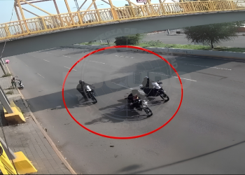 Three motorcyclists riding in a tight circle on a wet road beneath a yellow pedestrian bridge. The scene is circled in red for emphasis.