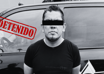 Man with a black bar over his eyes stands in front of a dark SUV; a red 'DETENIDO' stamp overlaying the image indicates detention.