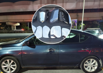 Blue sedan parked on the street with a severely cracked front windshield, shown in a zoomed circular inset highlighting the shattered glass from an impact.