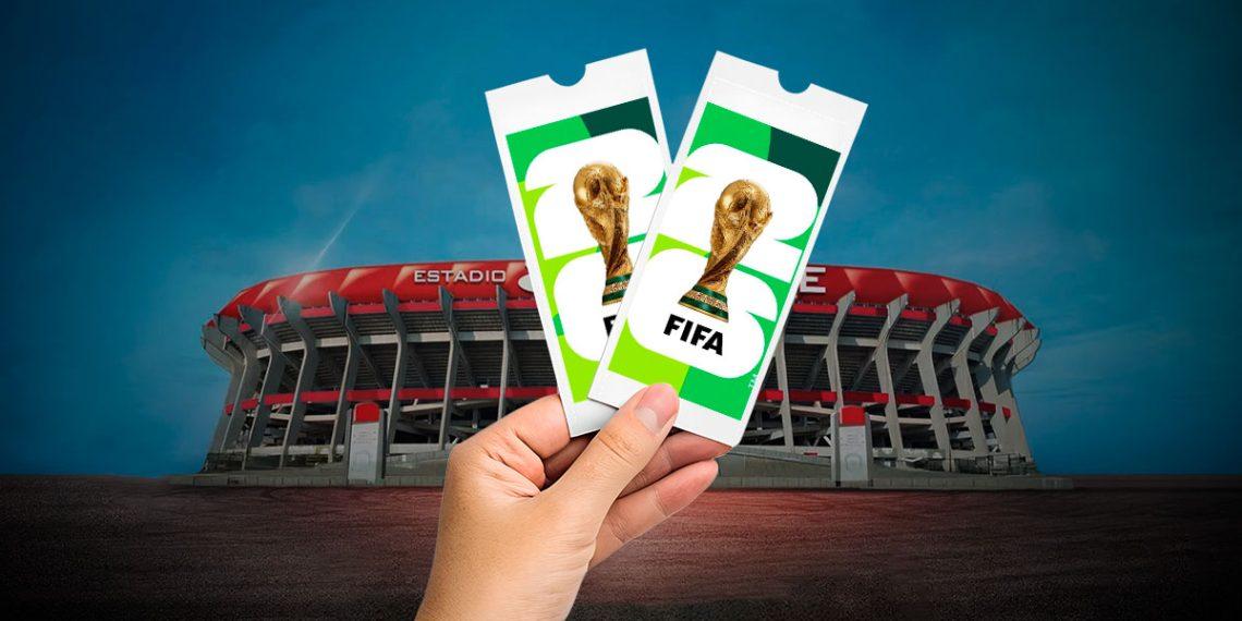 Hand holding two FIFA World Cup tickets in front of a large football stadium against a blue sky, suggesting event access.