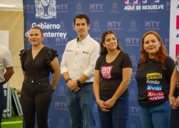Four adults stand in a line for a photo at a public event, with a blue branded backdrop behind them.